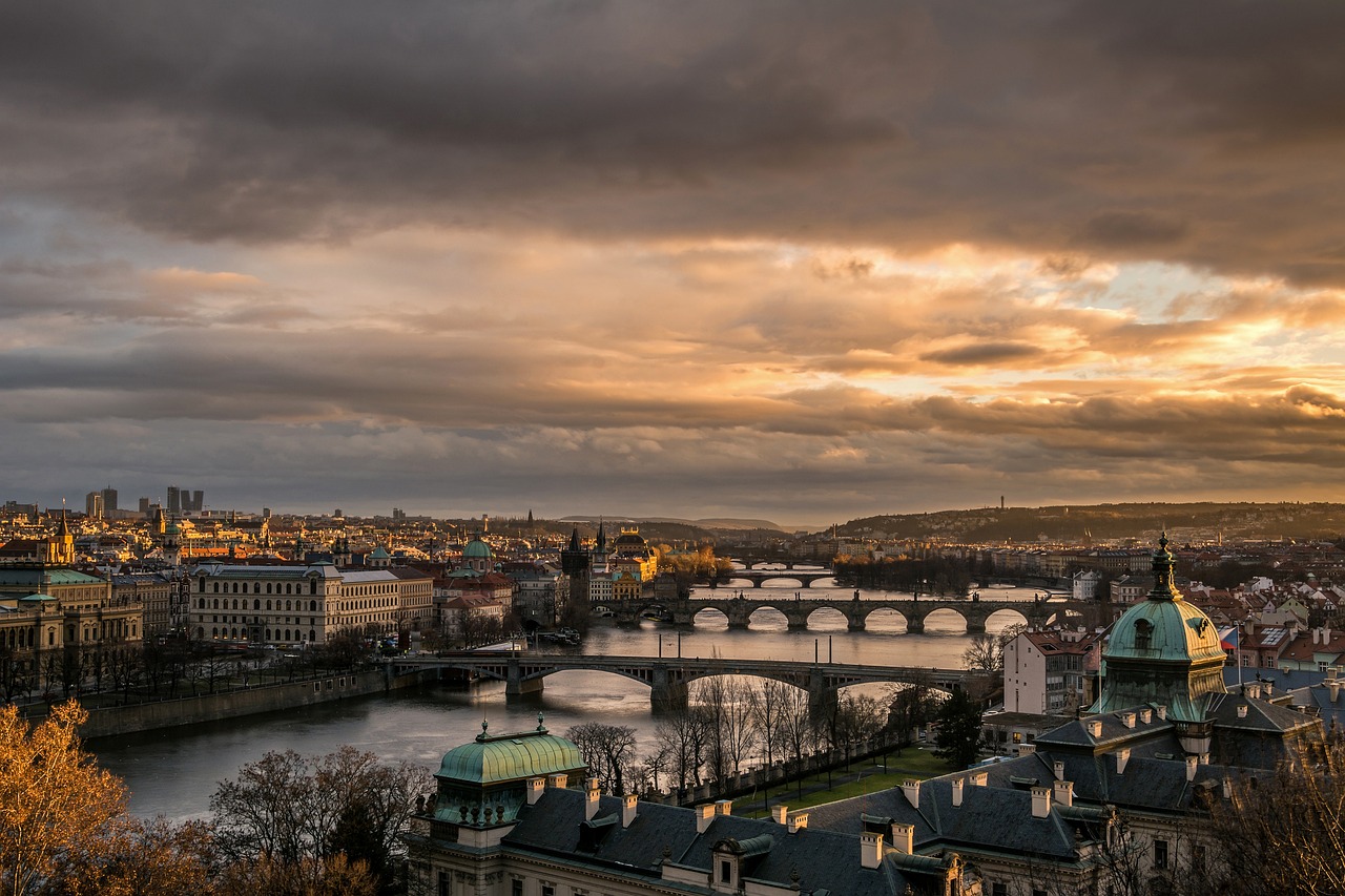 Das Bild zeigt Prag in der Vogelperspektive. Man sieht die historische Stadt und die Brücken in der Abenddämmerung.